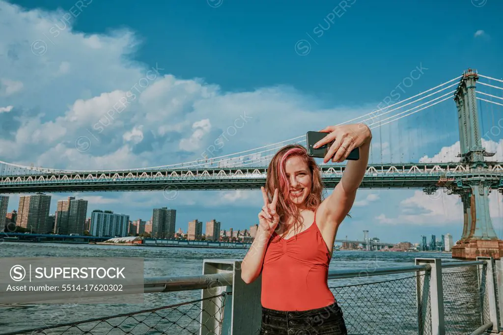 Young woman standing by river taking selfie.