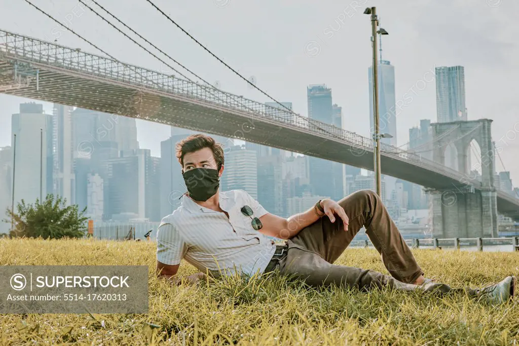 Young man sitting in park wearing face mask.