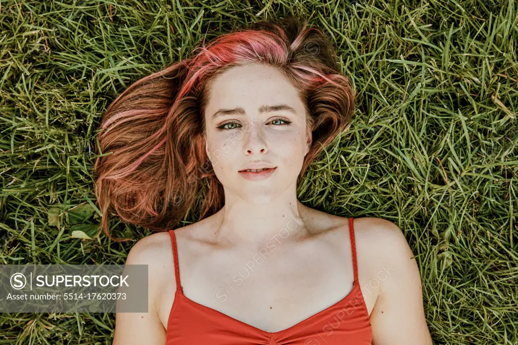 Portrait of young woman lying outdoors on grass.