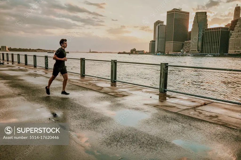 Male athlete running on waterfront during sunset.