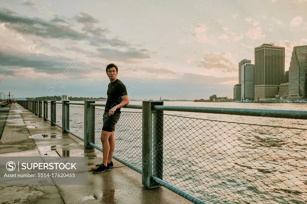Male athlete relaxing on waterfront during sunset.
