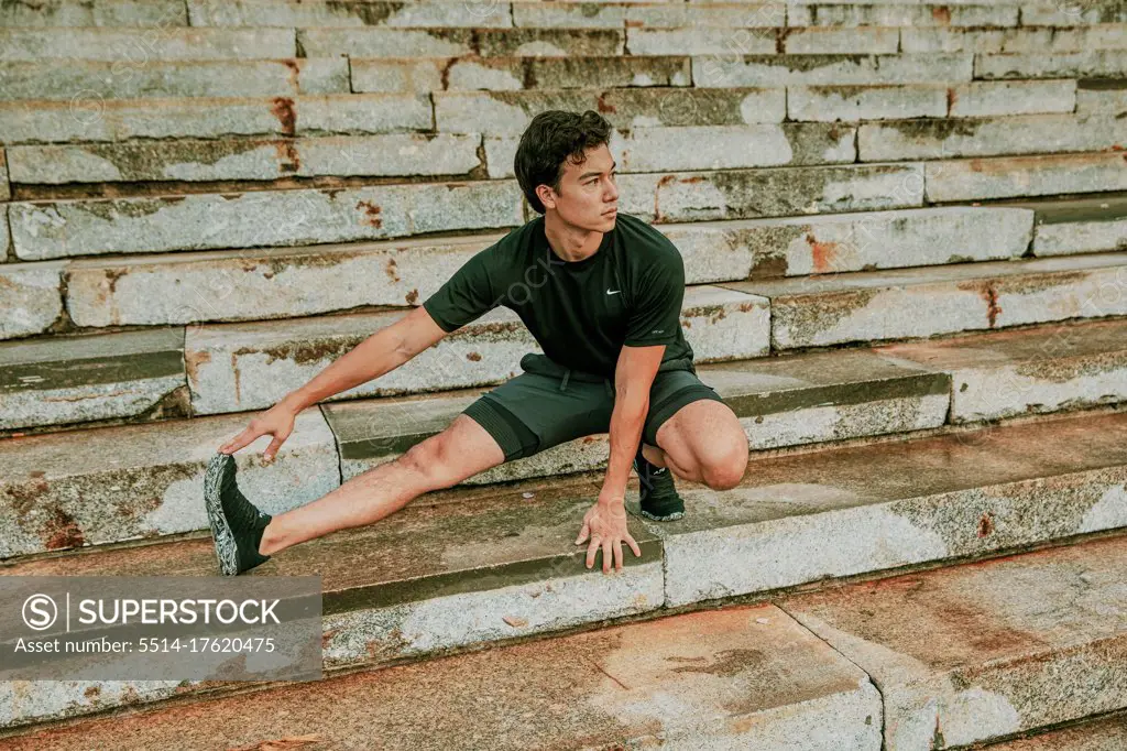 Male athlete stretching on steps during sunset.