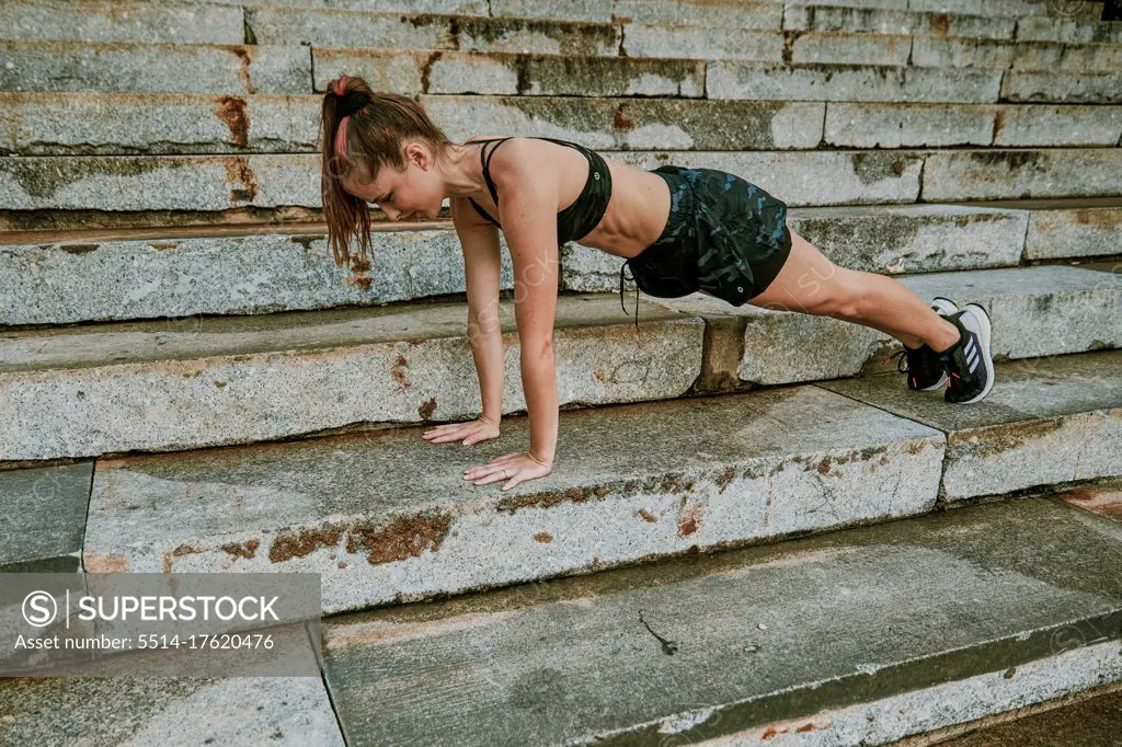 Female athlete stretching on steps during sunset.