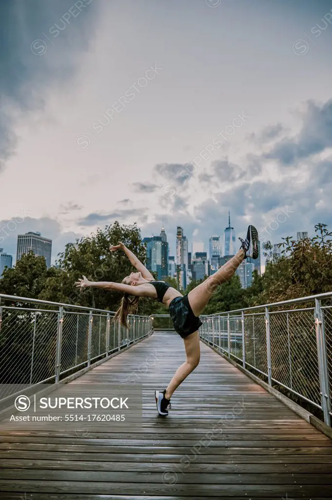 Female athlete stretching by city park during sunset.