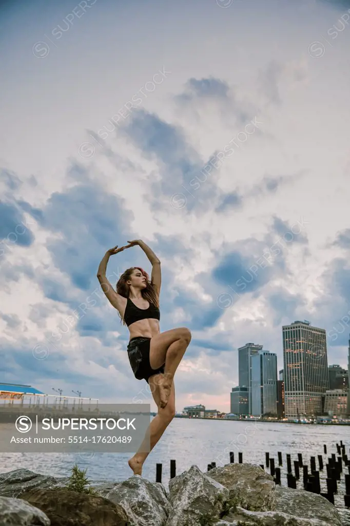 Young athlete dancing during sunset by city skyline.
