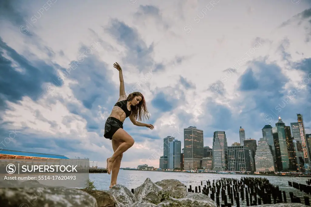 Young athlete dancing during sunset by city skyline.