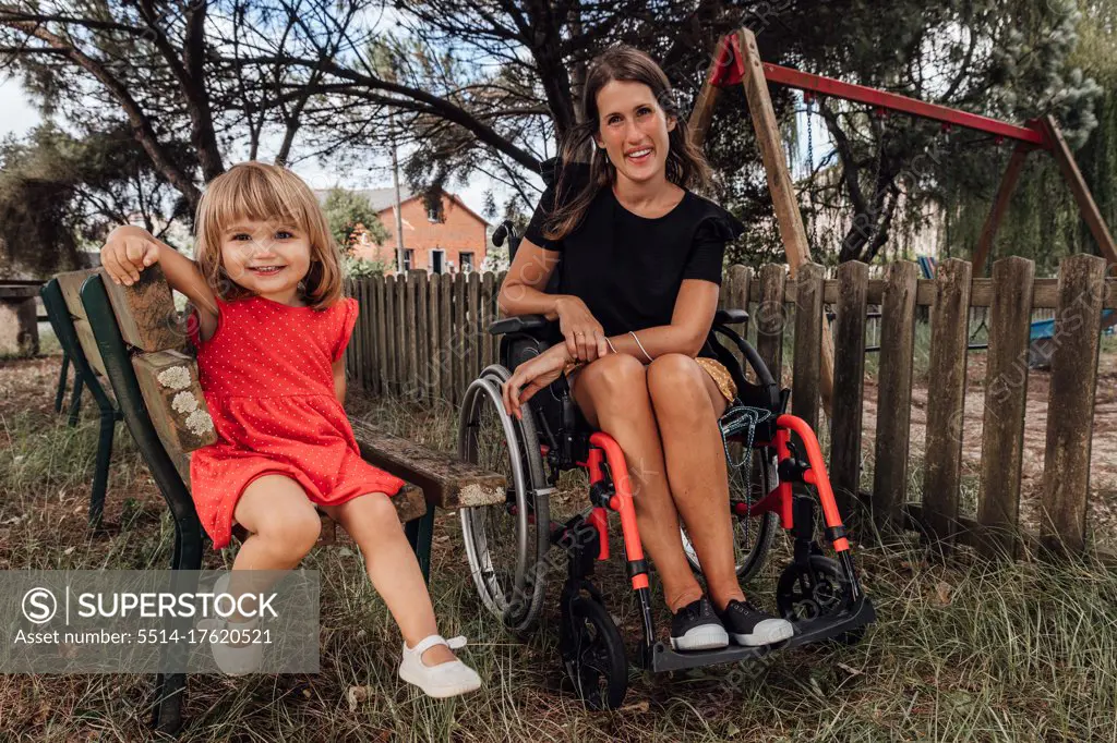 Portrait of little girl smiling next to her mother in a wheelchair in