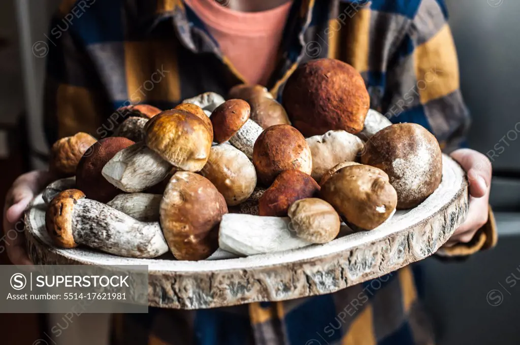 A large wooden dish with fresh forest mushrooms in children's hands.