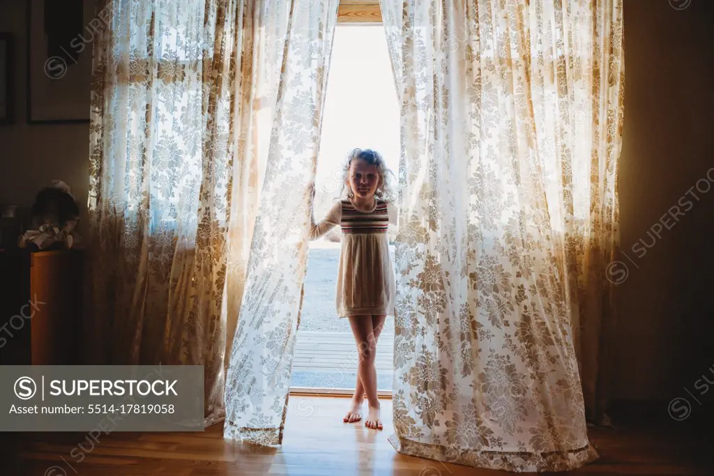 Young girl standing in between vintage curtains bored during isolation