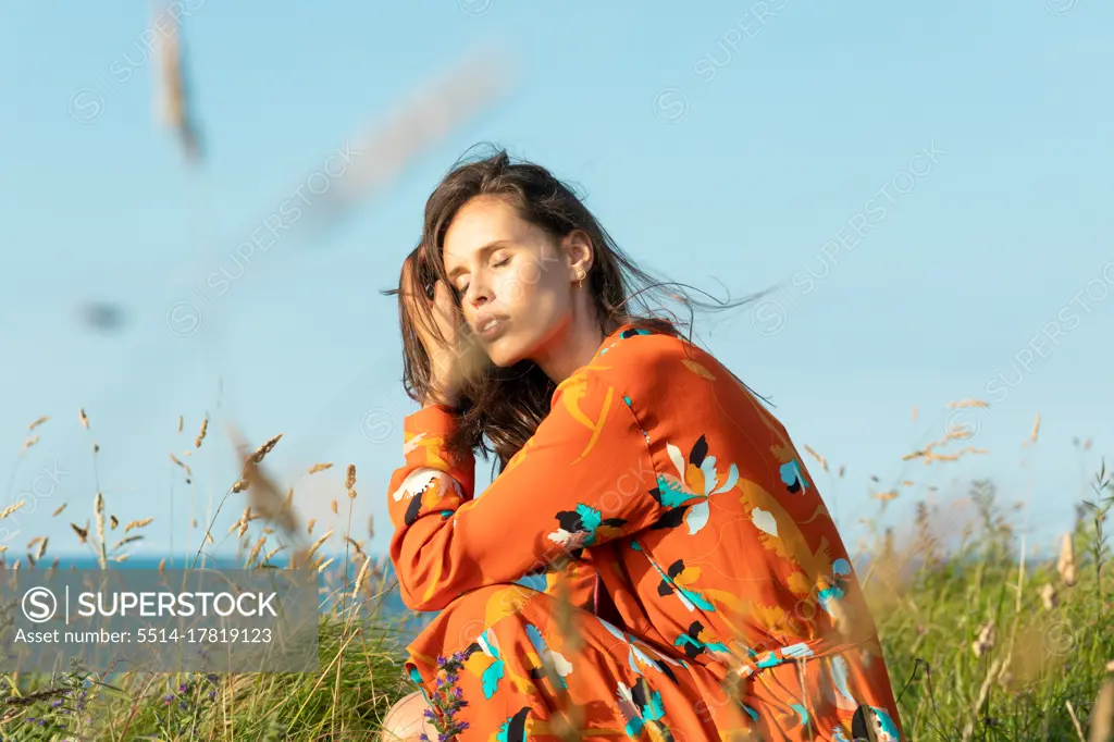 Young woman with long hair and flowery fashion orange dress posing by