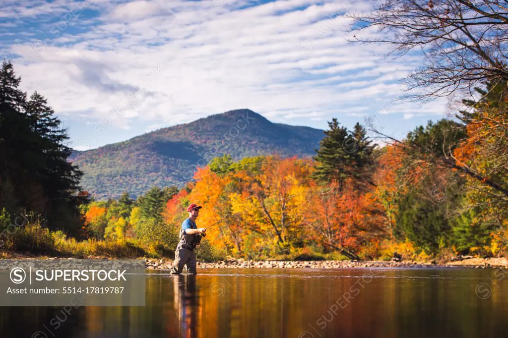 Fly-fisherman casting in river with foliage and reflections