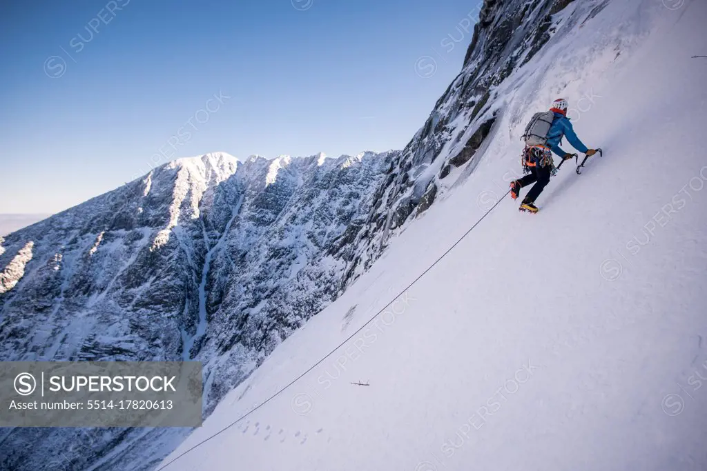 Alpine climber ascending steep snow with mountains behind