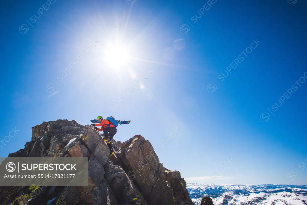 Man with skis on back climbing to summit of mountain