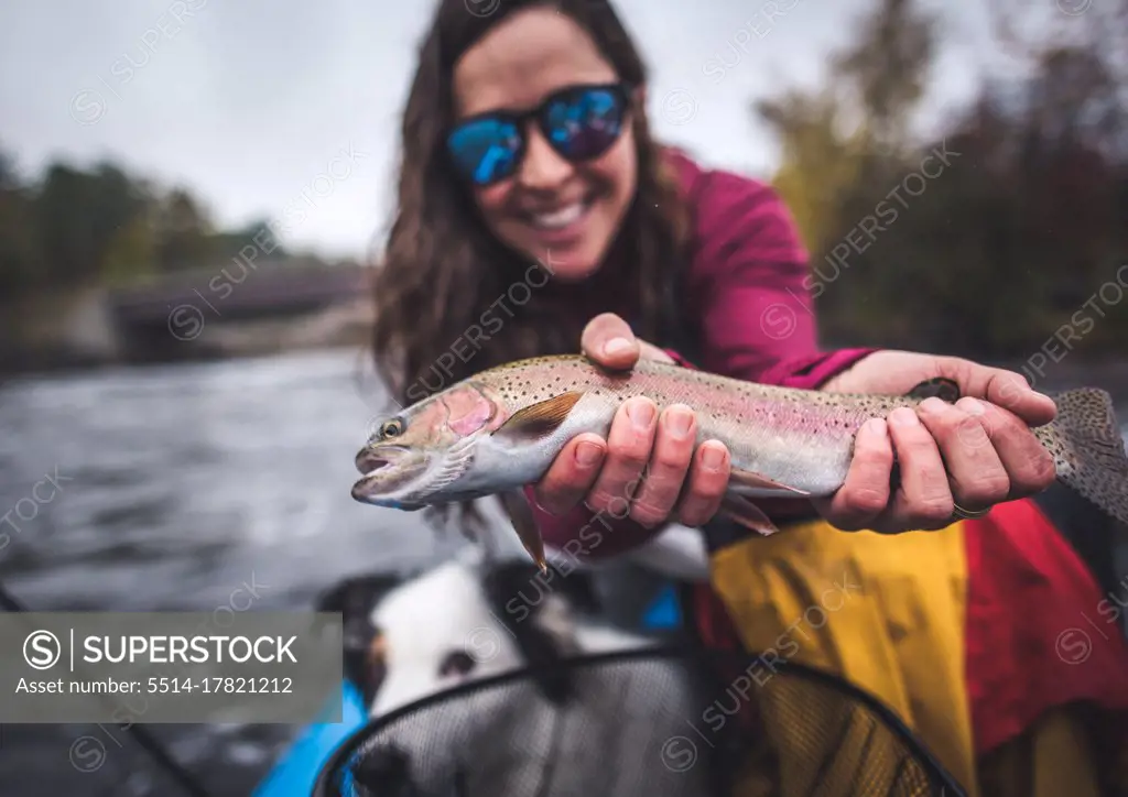 Woman smiling while holding a rainbow trout in boat