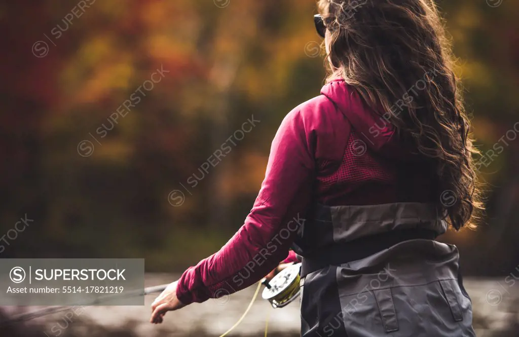 Woman in waders casting in river with fall foliage behind her