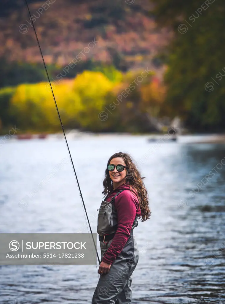 Woman in waders standing in river with fall foliage behind