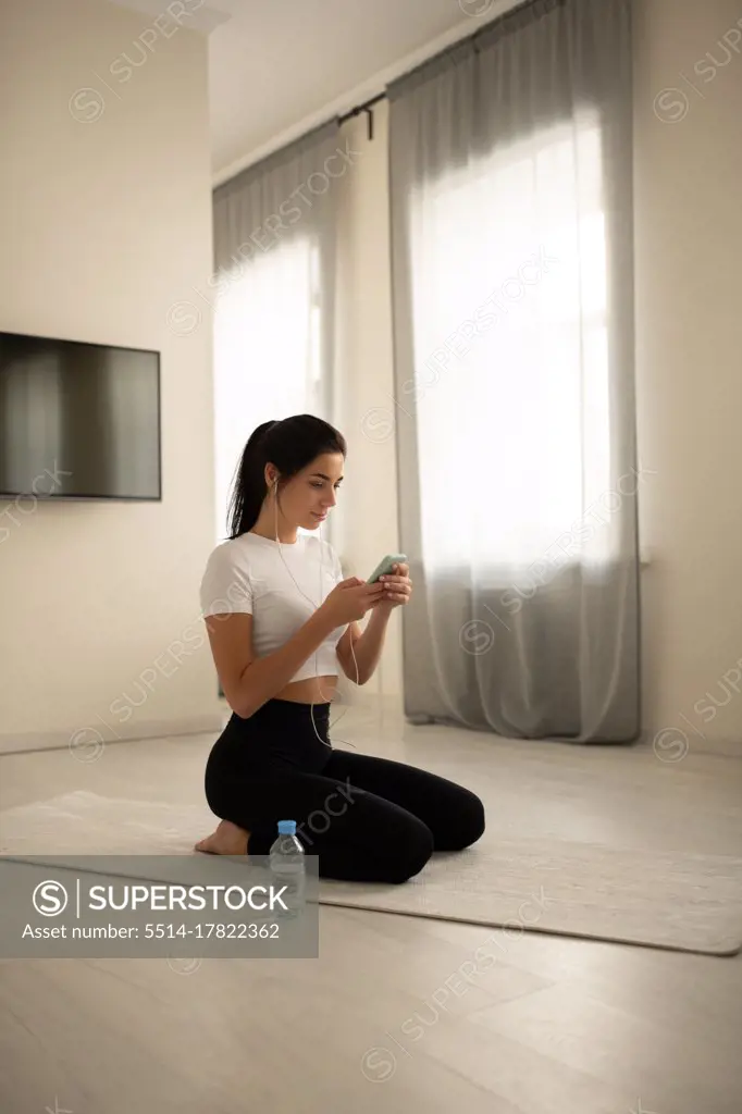 Female sitting on mat and browsing smartphone