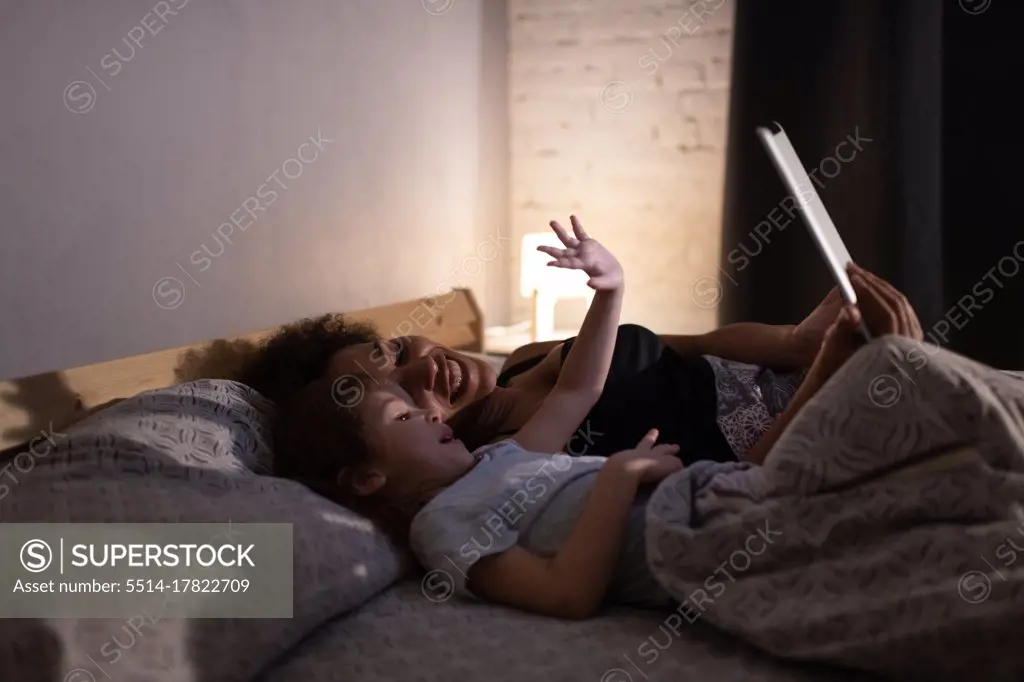Happy ethnic mother and daughter making video call in evening