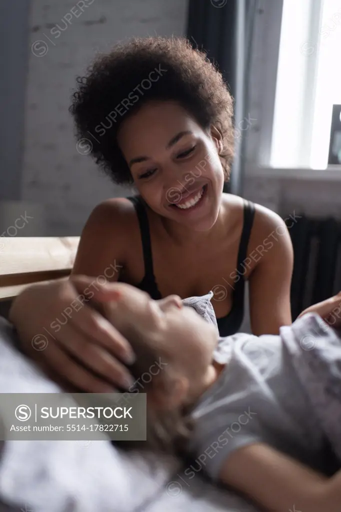 Happy ethnic mother waking up daughter in morning