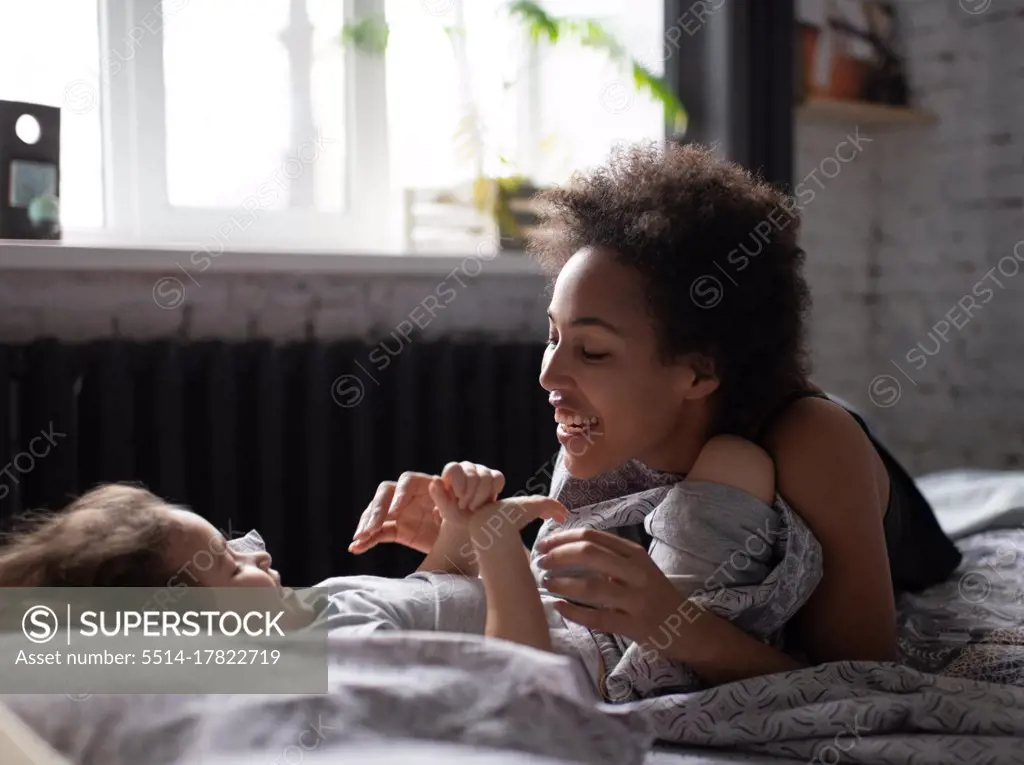 Ethnic mother playing with daughter after awakening
