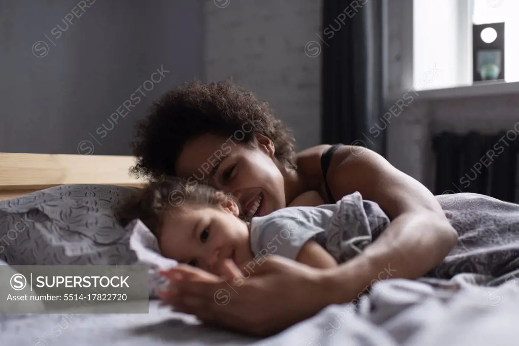 Cheerful mixed race mother and daughter lying on bed in morning