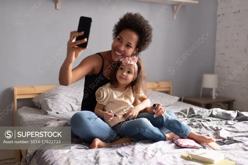 Cheerful ethnic mother with daughter making video call on smartphone