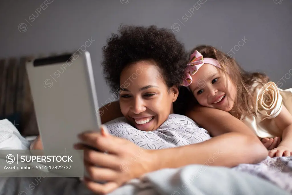 Mixed race mother and daughter making video call on bed