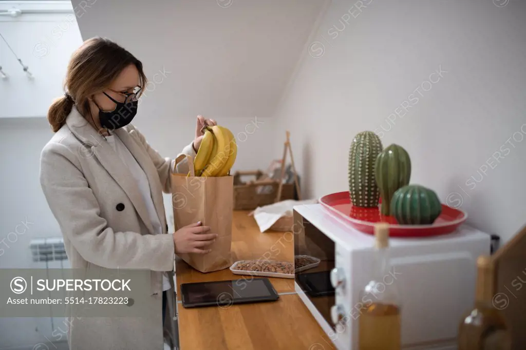 Woman in mask taking purchases from bag at home