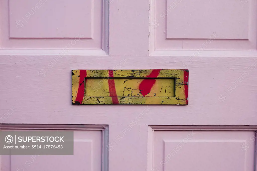 detail of a pink door with an old yellow-colored mailbox or letterbox sprayed with red