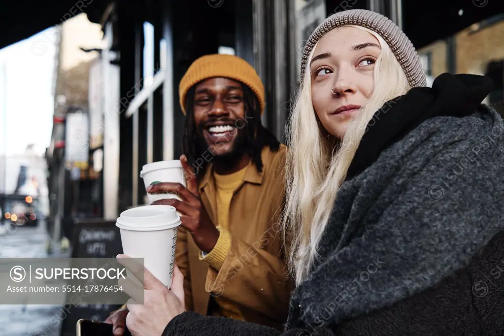 multiracial couple sitting outdoors laughing while drinking coffee. biracial lovers on a date concept.