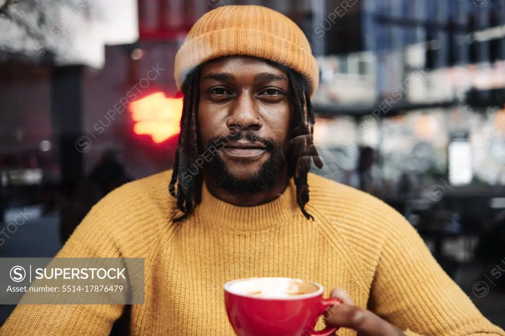 african male holding a cup of coffee while staring at the camera, reflection of the city on window