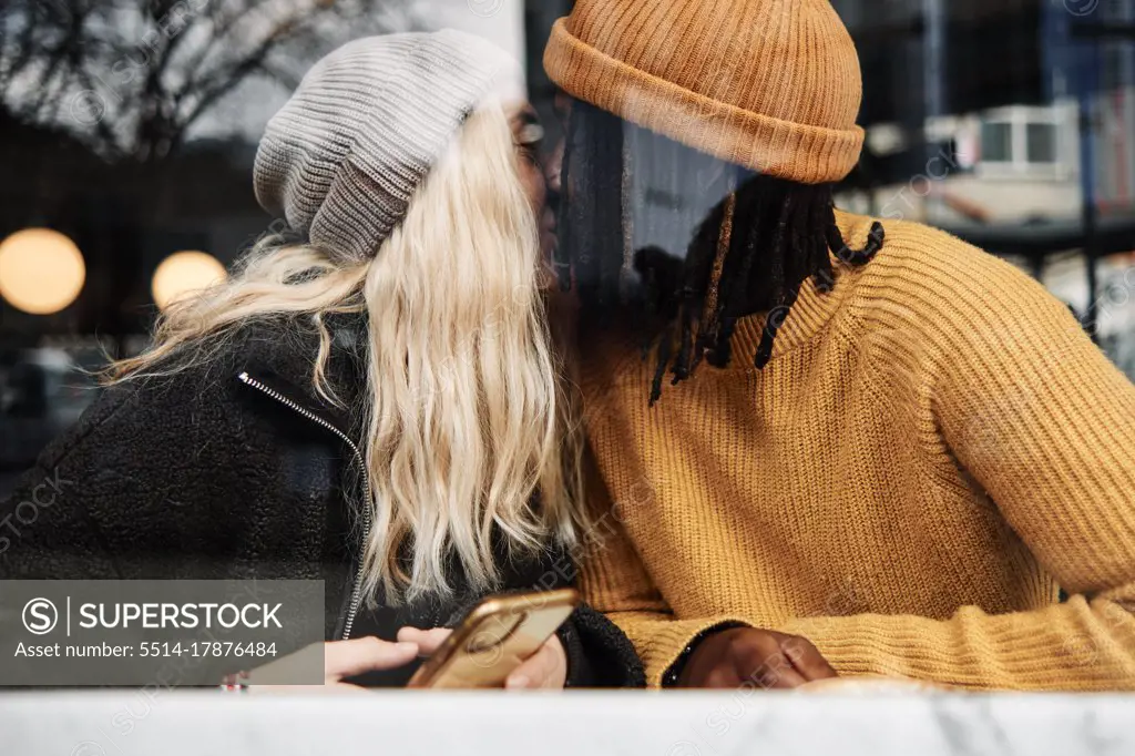 happy biracial couple kissing at the window of a cafe, reflection on the glass