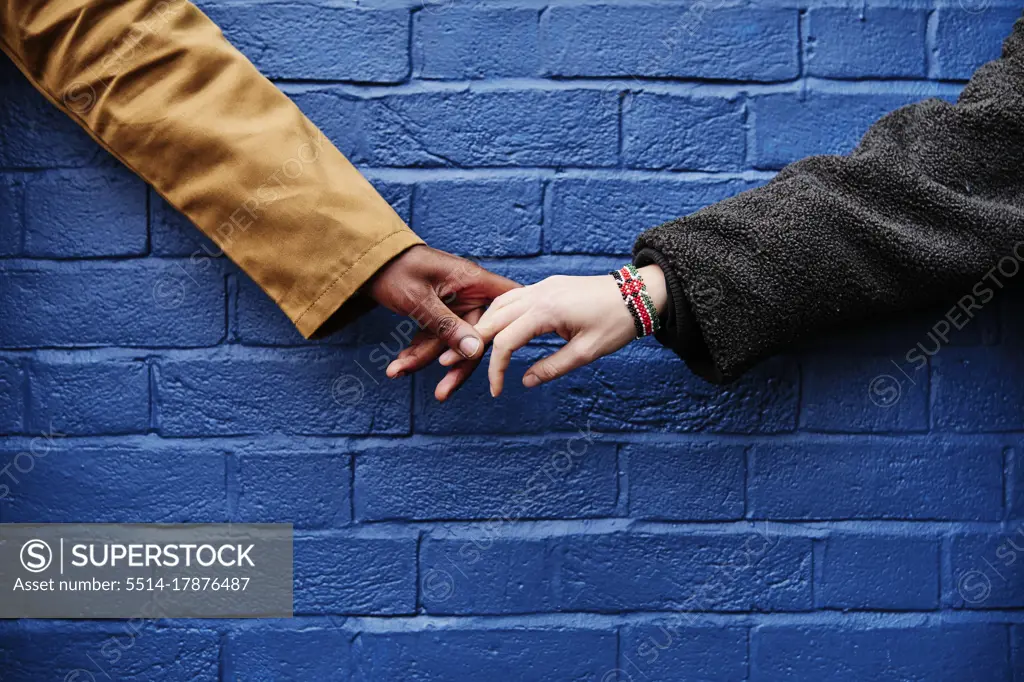 interracial couple holding hands, blue wall background. love symbolic concept.