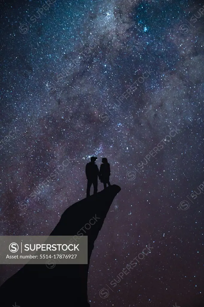 Couple standing on a cliff with the stars on the background