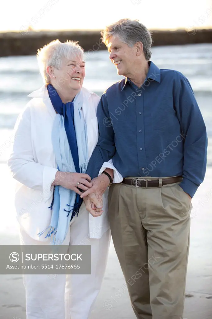 Portrait of older married couple holding hands and laughing at Beach