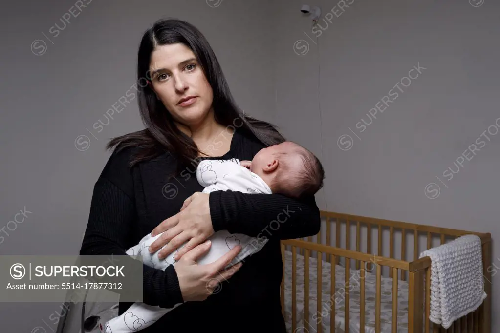 Calm woman hugging tiny newborn kid while standing in nursery