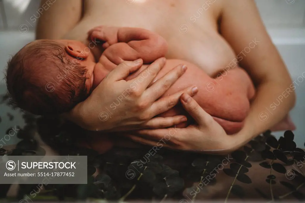 Mother holding newborn baby breastfeeding in bath tub after birth