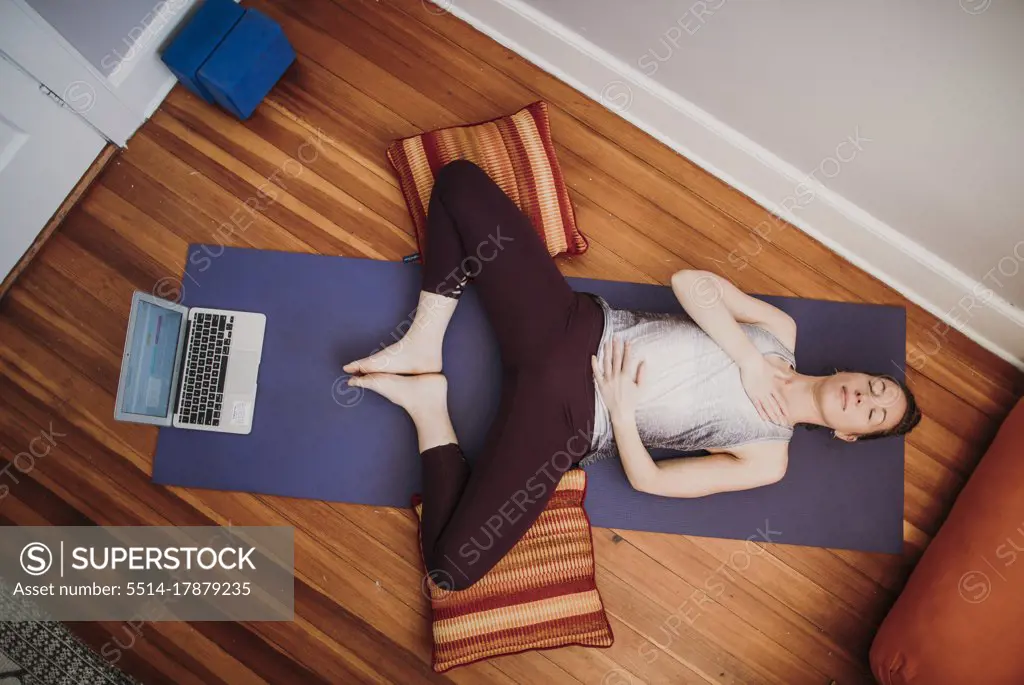 Woman in athletic wear with laptop computer relaxes on floor of home