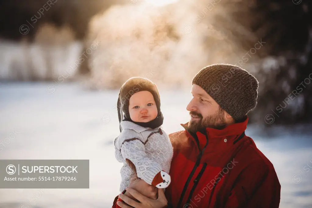 Dad and beautiful baby outside in snow in winter during golden sunset