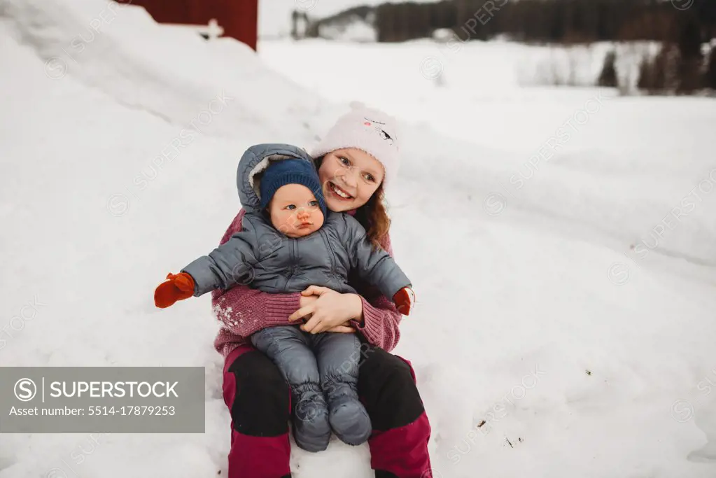 Smiley Big sister holding baby brother outside in the snow on cold da