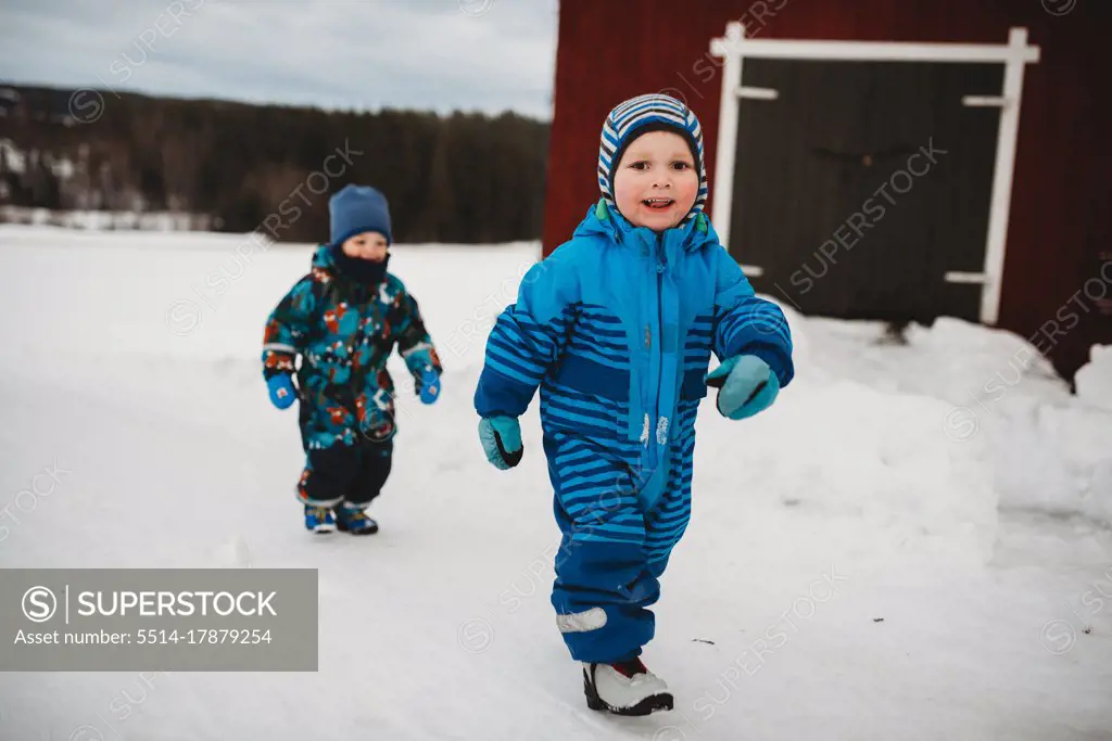 Young twin boys smiling walking in snow in Scandinavian farm by barn