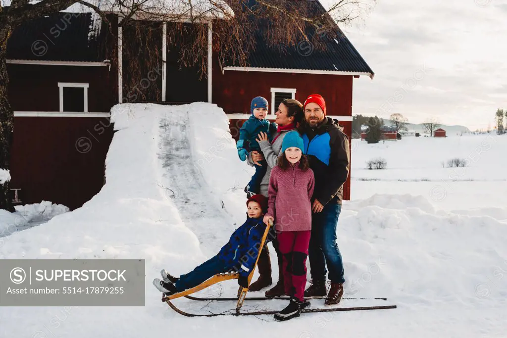 Beautiful family standing by red barn in Norwegian countryside in snow