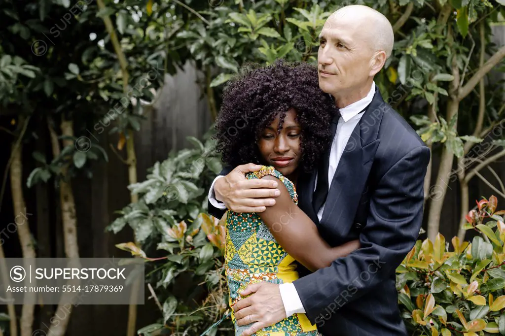 Interracial affectionate happy couple hugging by garden