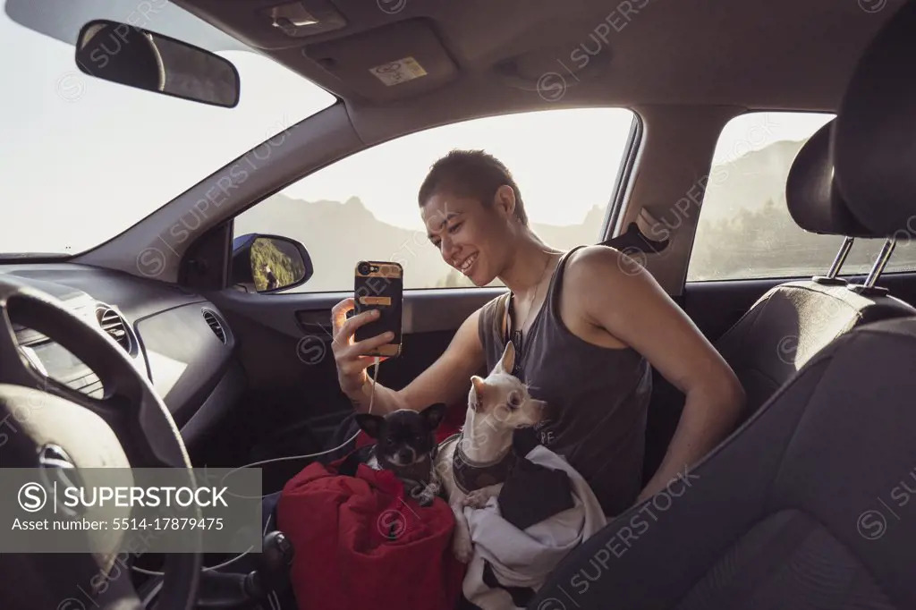 Happy person with two dogs on lap in car takes photos with phone spain