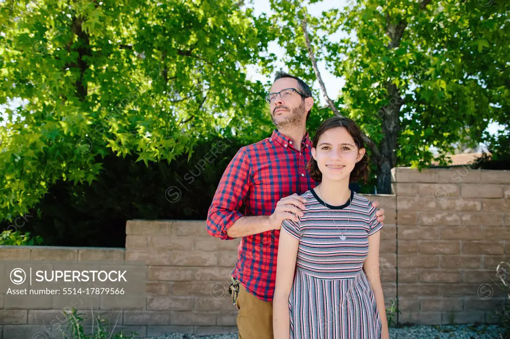 Proud Father With Hands On Her Shoulders Stands Behind Teen Daughter