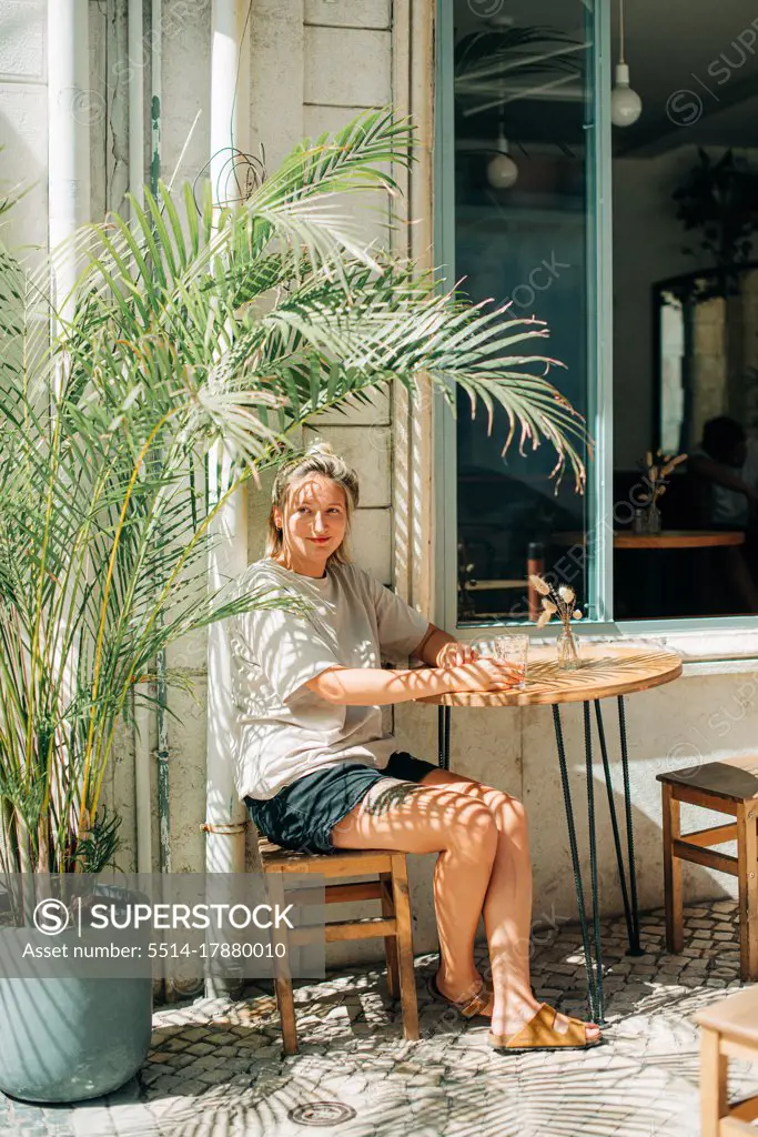 Woman sitting in outdoor cafe in shade of palm tree during summer day