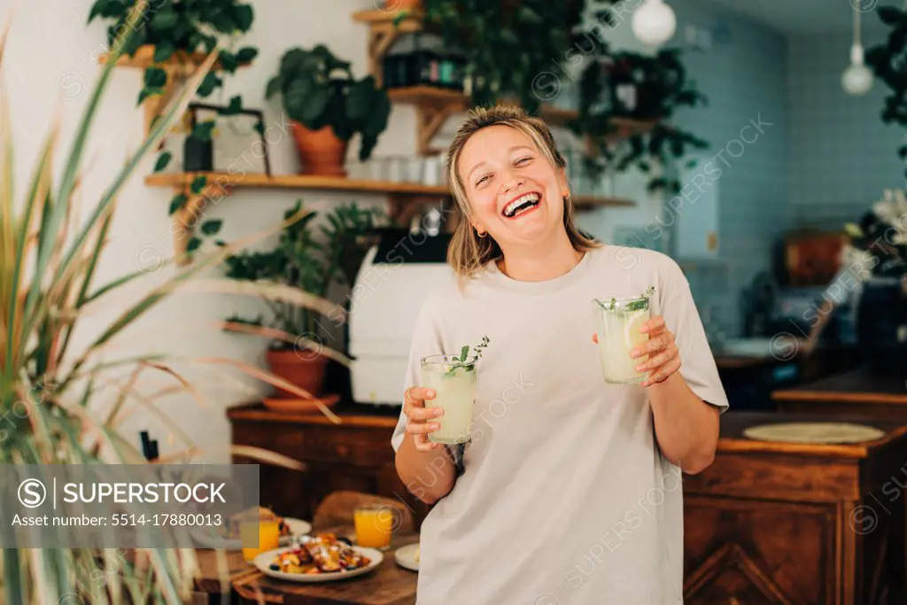 Woman with lemonade laughing at camera while standing in cafe