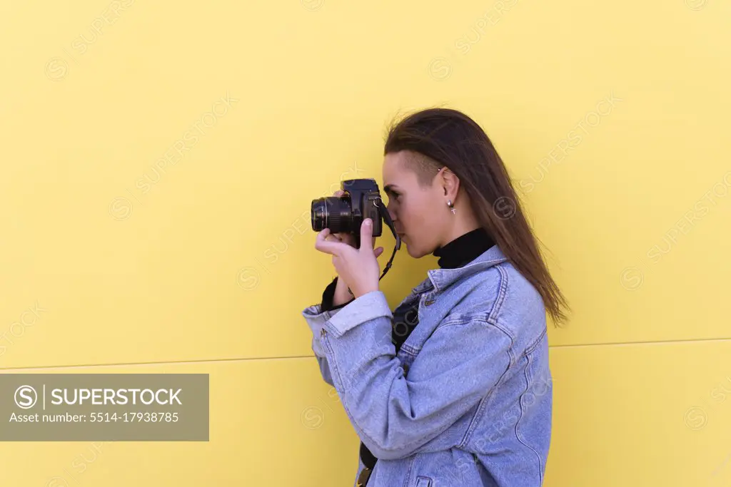 Young girl dressed in modern clothes uses her photo camera. Yell