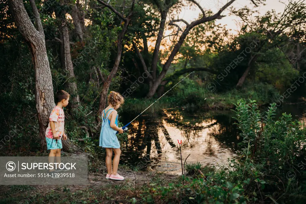 Brother and sister reeling fishing pole out of water at sunset