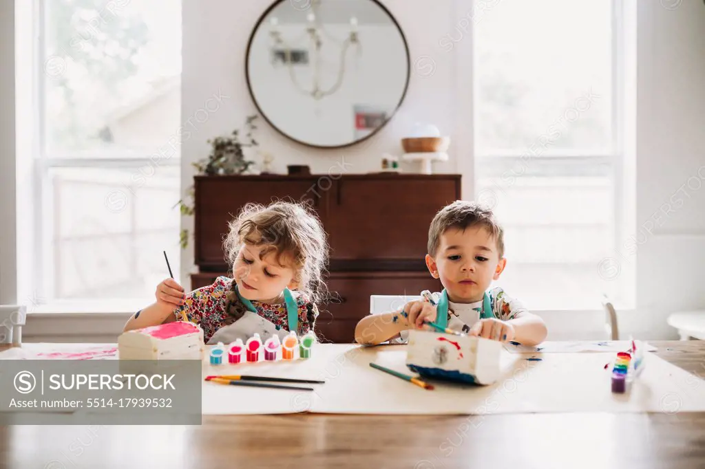 Young siblings sitting painting colorful boxes in modern dining room